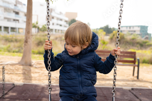 The child is riding on a swing. Boy playing outside