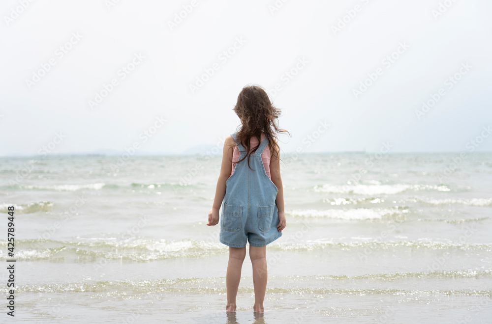 Back view of child Asian girl relaxing on the beach having fun on summer vacation.