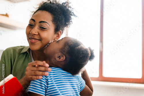 Black smiling girl kissing her happy mother at home kitchen © Drobot Dean
