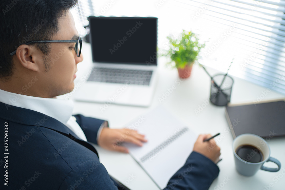 Young Asian businessmen are using a laptop and taking notes on the white desk in the office