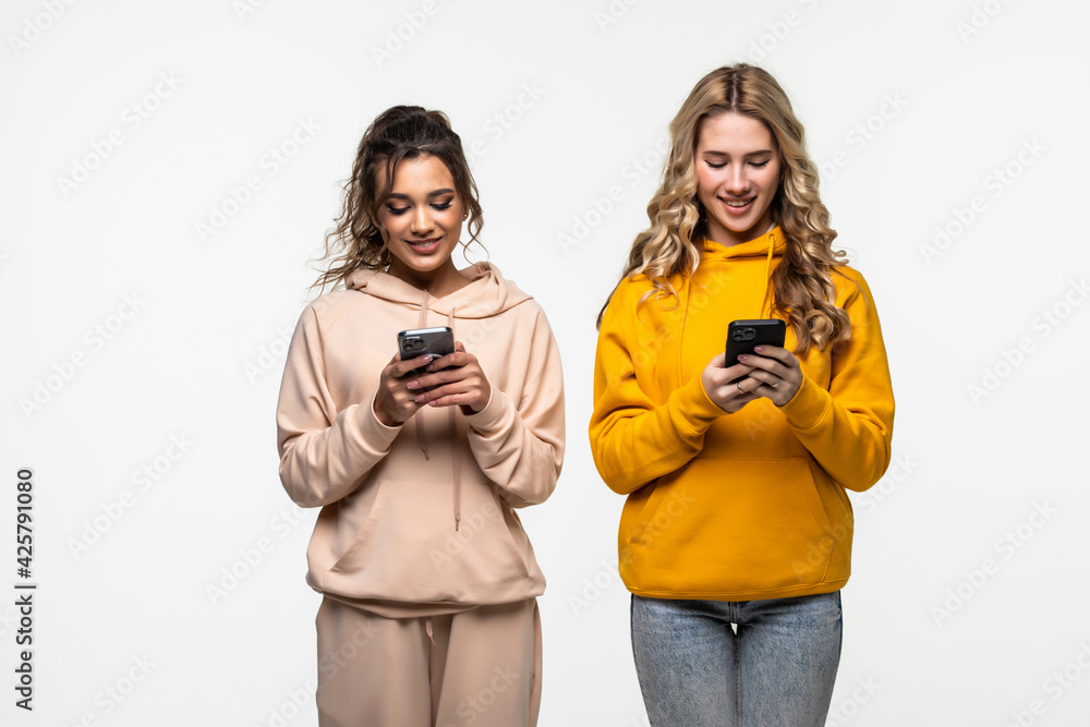 Two women looking in smartphone in social networks isolated over white background Two women looking in smartphone in social networks isolated over white background