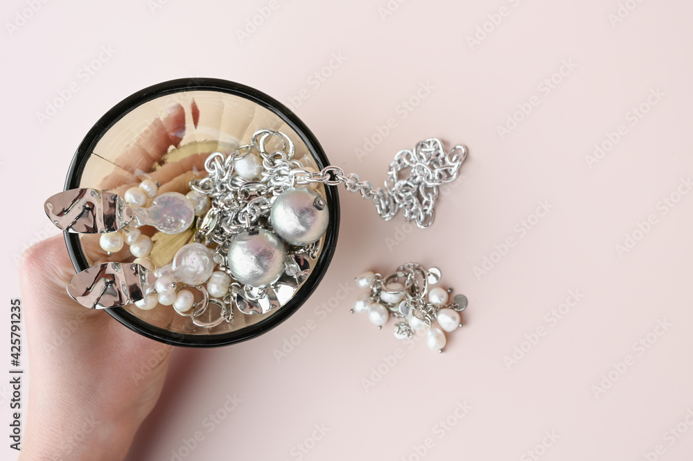 Glass goblet with stylish jewelry set of different earrings and chains in women's hand. Creative idea of jewelry display Glass goblet with stylish jewelry set of different earrings and chains in women's hand. Creative idea of jewelry display