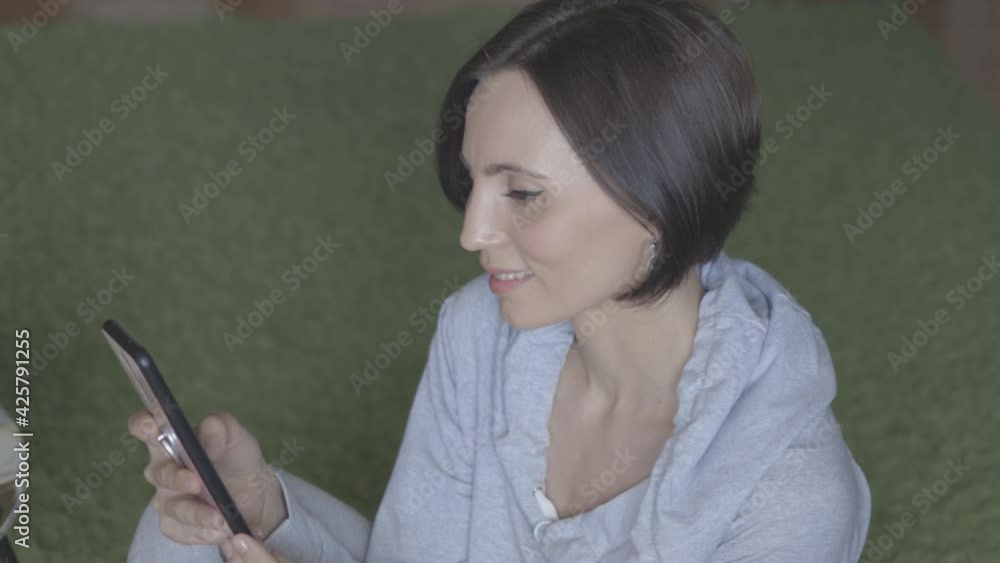 Woman with short hair, in grey clothes sitting sideways and looking in mobile.Surfing Internet Watching Content Videos Blogs Woman with short hair, in grey clothes sitting sideways and looking in mobile.Surfing Internet Watching Content Videos Blogs