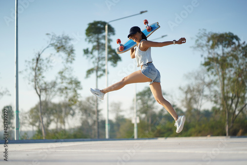 Asian women hold surf skate or skateboard outdoors and jumping on beautiful summer day. © phonix_a