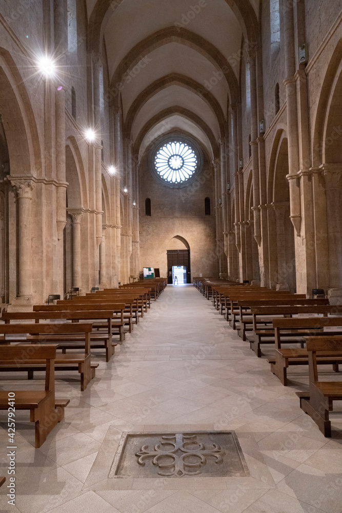 Obraz premium Abbazia medievale con rosone sullo sfondo in alto di 24 colonnine in controluce , in basso una croce bassorilievo , inquadratura verticale con illuminazione artificiale sui pilastri , con archi