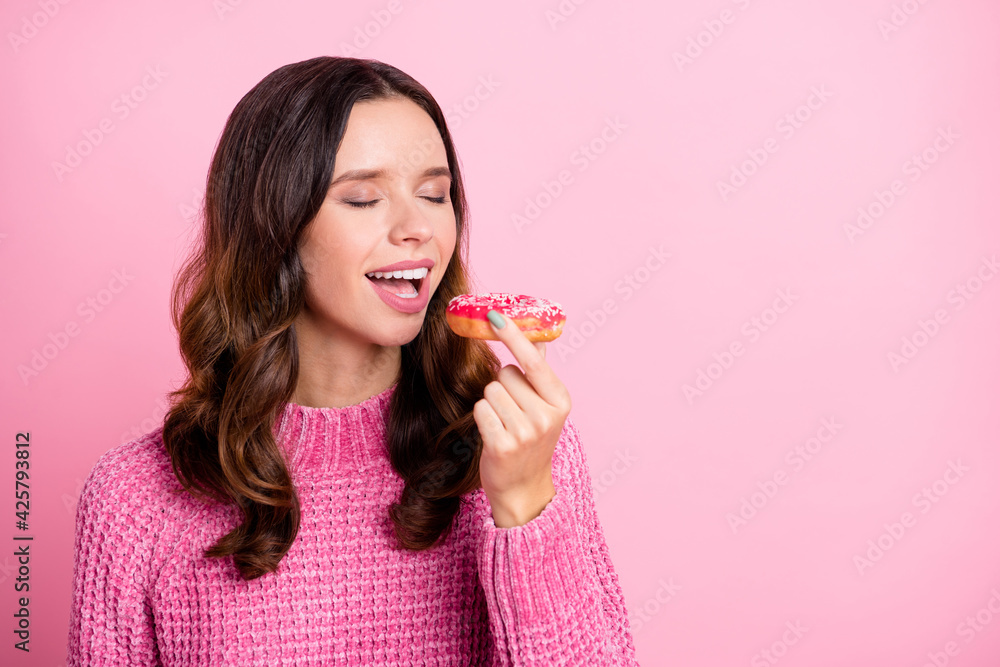 Portrait of attractive dreamy wavy-haired girl biting fresh baked donut copy space isolated over pink pastel color background Portrait of attractive dreamy wavy-haired girl biting fresh baked donut copy space isolated over pink pastel color background