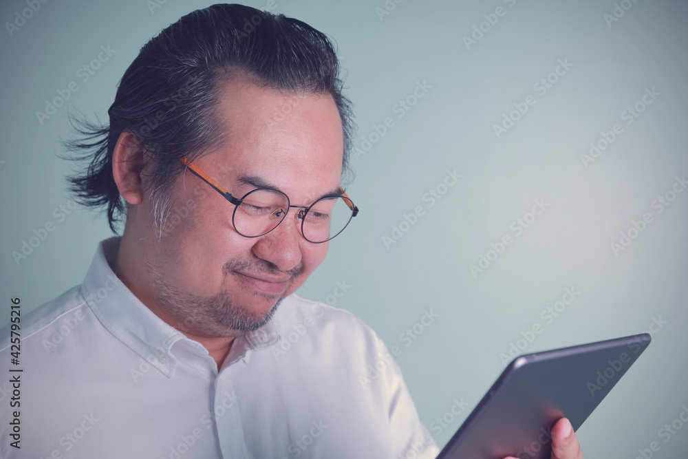 Close-up portrait Asian businessman wearing a white shirt and glasses looking at the tablet smile happy on green background. Concept business, technology, internet next-work. Close-up portrait Asian businessman wearing a white shirt and glasses looking at the tablet smile happy on green background. Concept business, technology, internet next-work.