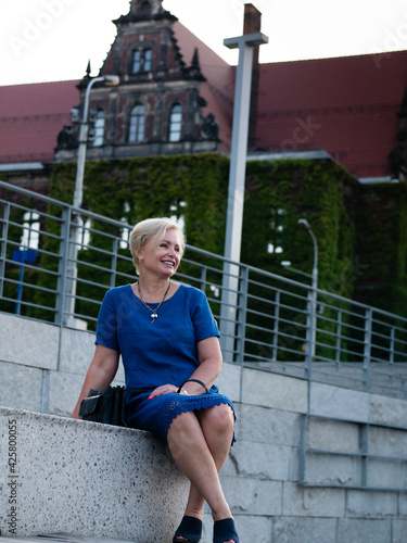 Happy elderly blonde woman in blue dress in summer park.