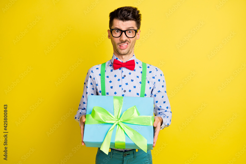 Portrait of attractive funny guy holding in hands giftbox grimacing disgust isolated over bright yellow color background Portrait of attractive funny guy holding in hands giftbox grimacing disgust isolated over bright yellow color background