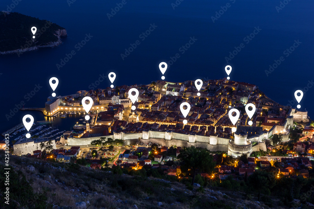 Fototapeta premium Map pin icons on Dubrovnik's cityscape at dusk. Walled Old Town of Dubrovnik in Croatia viewed from above at night.