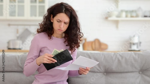 No money left. Unhappy sad girl holding last cash money in wallet, papers calculate domestic bills at home. Millennial woman frustrated about lack of finances, feeling anxiety about debt or bankruptcy