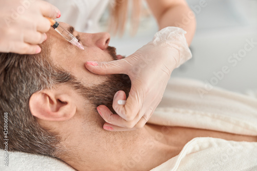 Close up treatment of young man by a beautician for tightening and smoothing wrinkles on the face skin. Mesotherapy injections to attractive male