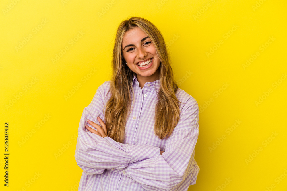 Young blonde caucasian woman isolated on yellow background who feels confident, crossing arms with determination. Young blonde caucasian woman isolated on yellow background who feels confident, crossing arms with determination.