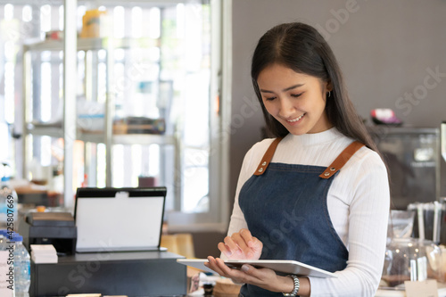 Young Asian owner or worker woman using digital tablet in coffee shop.
