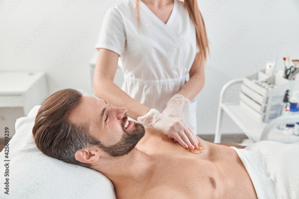 Woman beautician put depilatory wax to chest of young man for hair removal. Depilation with wax Woman beautician put depilatory wax to chest of young man for hair removal. Depilation with wax