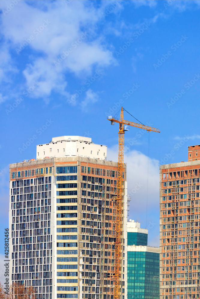 Fragment of construction of modern residential skyscrapers by tower crane on a background of blue sky.