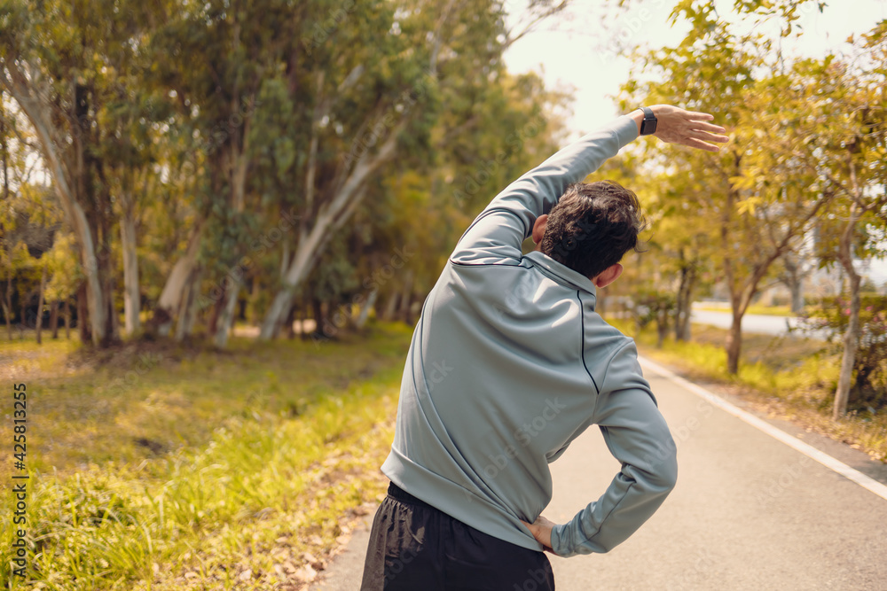 young man stretching in the park before running. Young man workout before fitness training at the park. Healthy and exercise young man warming up on the road beside the forest.