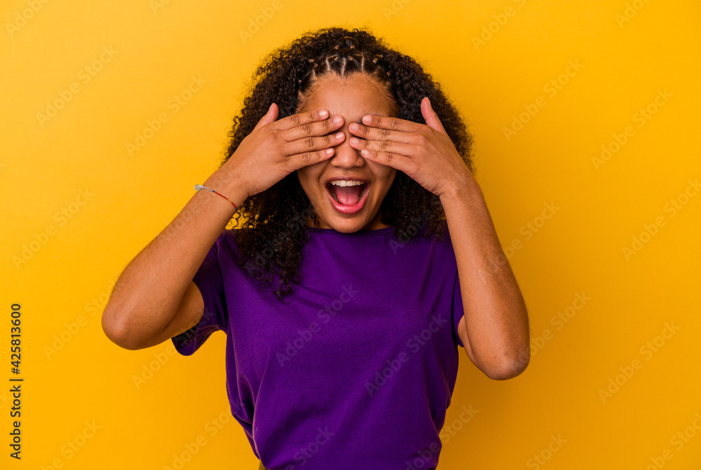 Young african american woman isolated on yellow background covers eyes with hands, smiles broadly waiting for a surprise. Young african american woman isolated on yellow background covers eyes with hands, smiles broadly waiting for a surprise.
