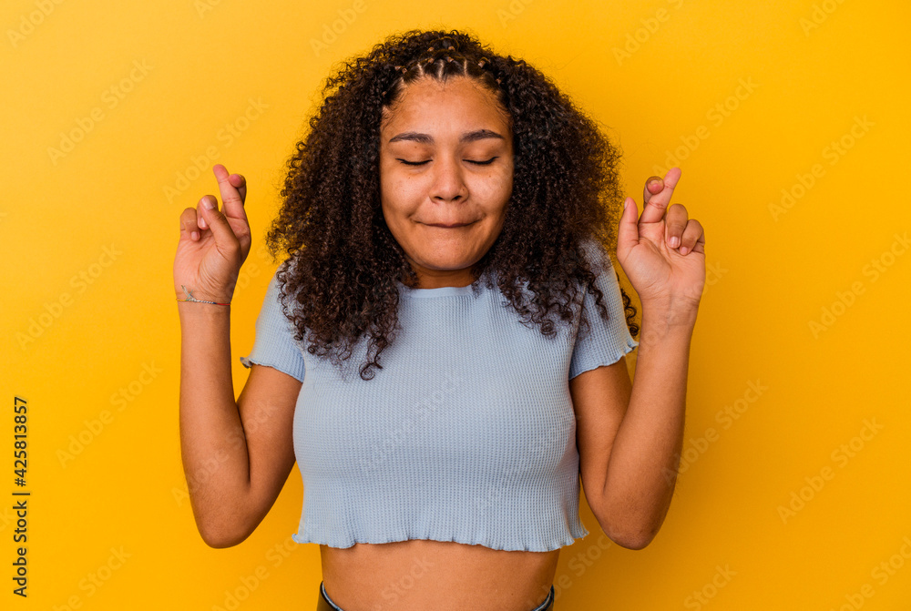 Young african american woman isolated on yellow background crossing fingers for having luck Young african american woman isolated on yellow background crossing fingers for having luck