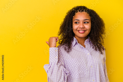 Young african american woman isolated on yellow background points with thumb finger away, laughing and carefree.