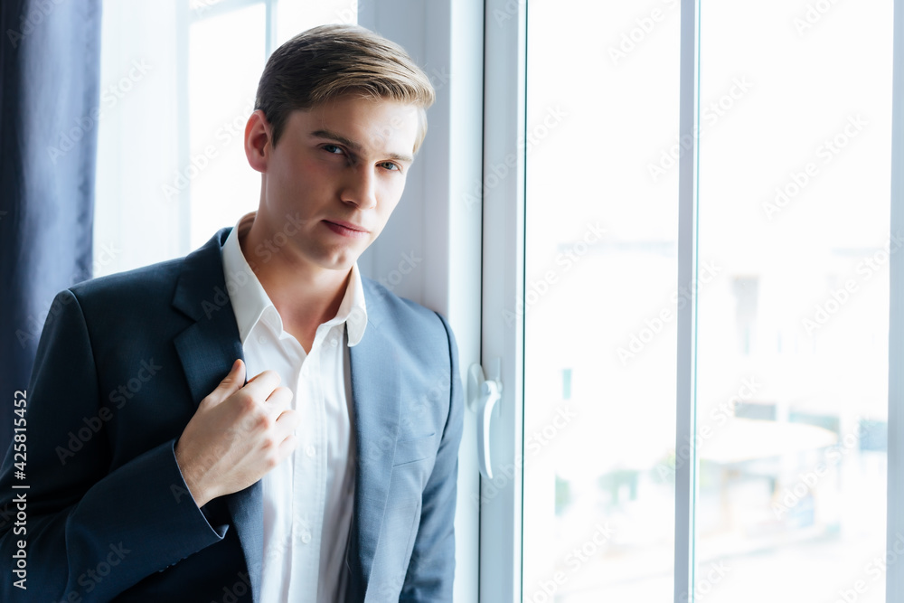 Confident business man stand near window at office wearing suit and shirt Portrait Handsome young Caucasian businessman He is British guy Executive male look at camera Attractive men stay at workplace Confident business man stand near window at office wearing suit and shirt Portrait Handsome young Caucasian businessman He is British guy Executive male look at camera Attractive men stay at workplace