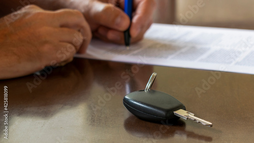detail of car key and on blurred background man signs car contract for rent or purchase. Buy or sell new or used vehicles. Car keys on the table. selective focus photo
