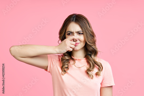 Smells bad, woman pinching nose with disgust on pink background