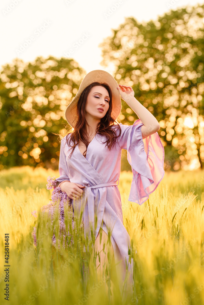 Stylish girl in violet dress and hat in field. Happy young woman on the sunset or sunrise in summer nature. Fashion and lifestyle concept. Stylish girl in violet dress and hat in field. Happy young woman on the sunset or sunrise in summer nature. Fashion and lifestyle concept.