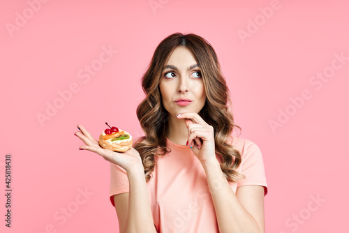 Dieting concept, confused pretty woman looking up holding pastry cake in hand
