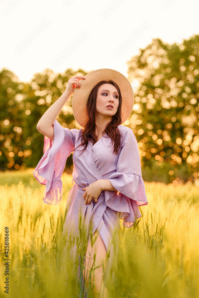 Stylish girl in violet dress and hat in field. Happy young woman on the sunset or sunrise in summer nature. Fashion and lifestyle concept. Stylish girl in violet dress and hat in field. Happy young woman on the sunset or sunrise in summer nature. Fashion and lifestyle concept.