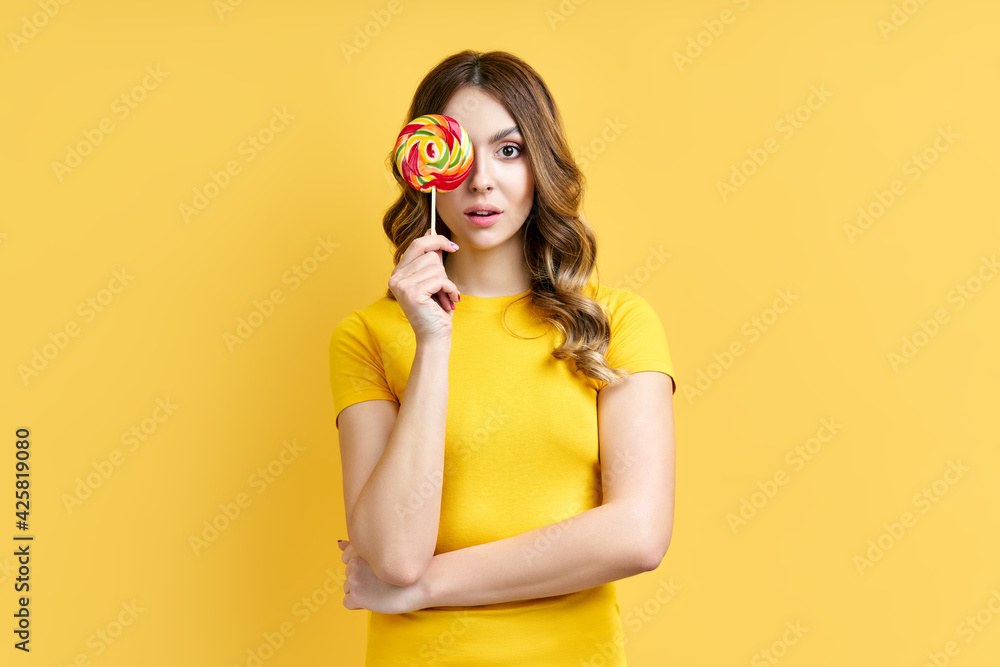 Obraz premium Pretty woman covers her eye with colorful lollipop isolated on y