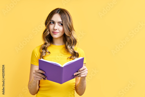 Dreamy positive girl rest with book on yellow background with copy space