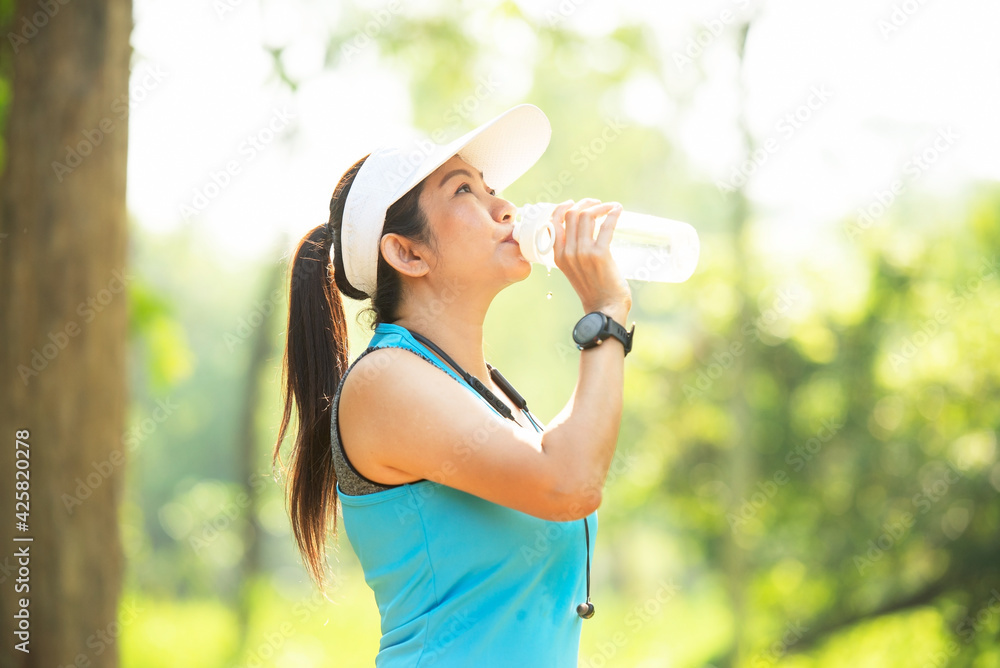 Healthy athletic woman drinking pure water after go running to be fresh in the nature park. Asian runner woman after exercise. Healthy and Lifestyle concept. On Nature background Healthy athletic woman drinking pure water after go running to be fresh in the nature park. Asian runner woman after exercise. Healthy and Lifestyle concept. On Nature background