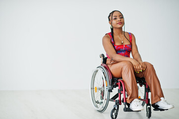 Young disabled African American woman in wheelchair against white wall.