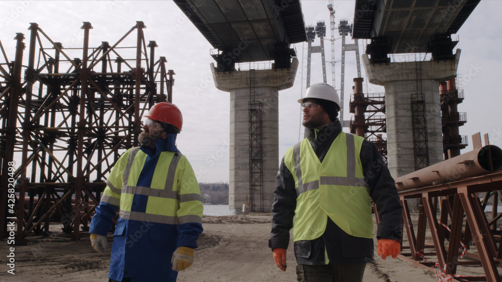 Male builders walking under bridge Male builders walking under bridge