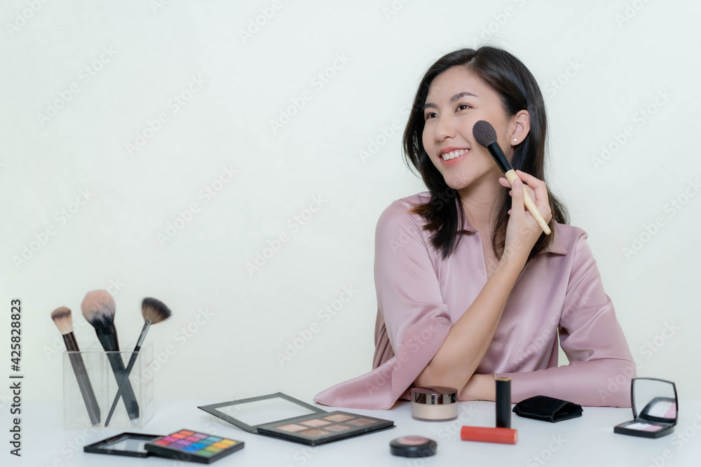 An Asian blogger beauty blogger shooting a video of herself wearing an orange lipstick in a studio. An Asian blogger beauty blogger shooting a video of herself wearing an orange lipstick in a studio.
