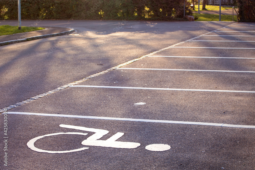 Empty parking lot, white lines on the asphalt, sunny day. Handicapped parking space at a parking lot outside a building, icon, sign painted on the designated parking space for disabled persons. Empty parking lot, white lines on the asphalt, sunny day. Handicapped parking space at a parking lot outside a building, icon, sign painted on the designated parking space for disabled persons.