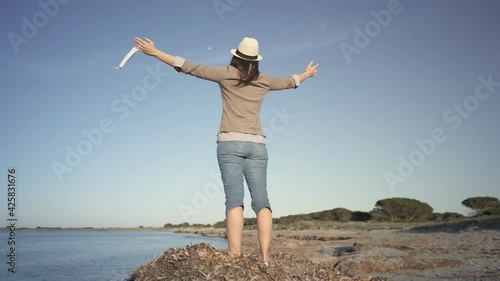 Unrecognizable young woman standing on beach near sea water in ocean resort with open arms holding medical mask just taken off. Hope for tourism business resumption due to end of Coronavirus pandemic