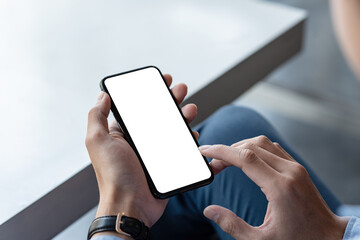 Close-up of a man hand holding a smartphone with a blank white screen at home. Mock up.