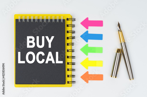 On a white background lies a pen, arrows and a notebook with the inscription - BUY LOCAL
