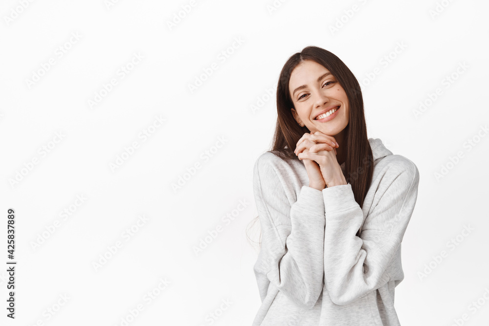 So adorable. Cute beautiful girl fascinated by something, holding hands near face and smiling, looking at lovely tender scene, watching romantic moment, standing over white background So adorable. Cute beautiful girl fascinated by something, holding hands near face and smiling, looking at lovely tender scene, watching romantic moment, standing over white background