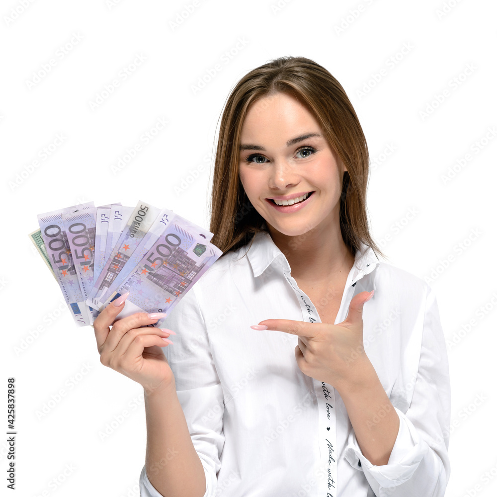 Smiling young pretty woman points at a stack of money. Isolated on white Smiling young pretty woman points at a stack of money. Isolated on white