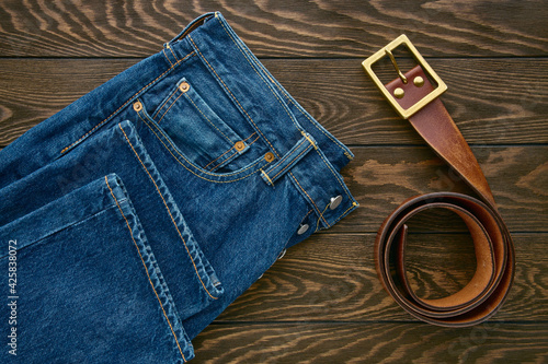 Detail of blue mens jeans and leather belt on wooden background