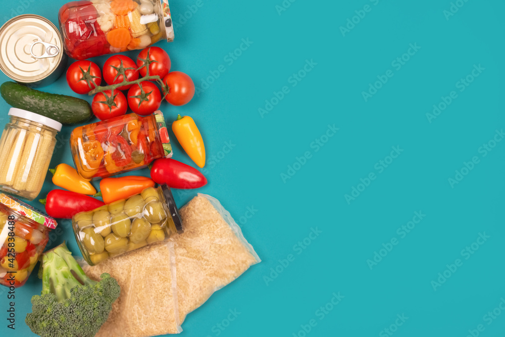 Different groceries, food donations on blue background with copy space - pasta, vegatables, canned food, baguette, cooking oil, tomatoes, cheese. Food bank, food delivery concept. Selective focus