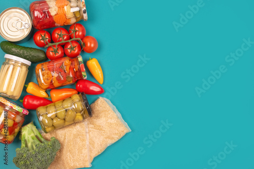 Different groceries, food donations on blue background with copy space - pasta, vegatables, canned food, baguette, cooking oil, tomatoes, cheese. Food bank, food delivery concept. Selective focus