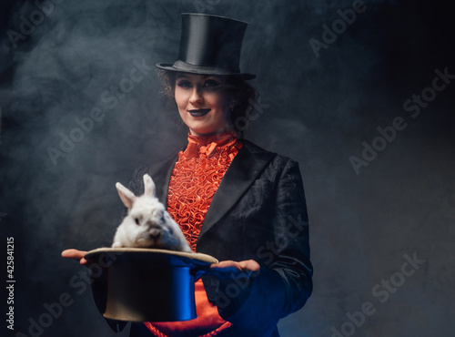 Attractive woman holding a top hat there is a white rabbit in smoke