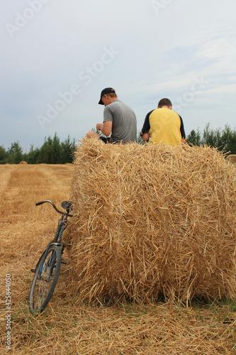 The guys are sitting on a haystack, next to him is a bicycle