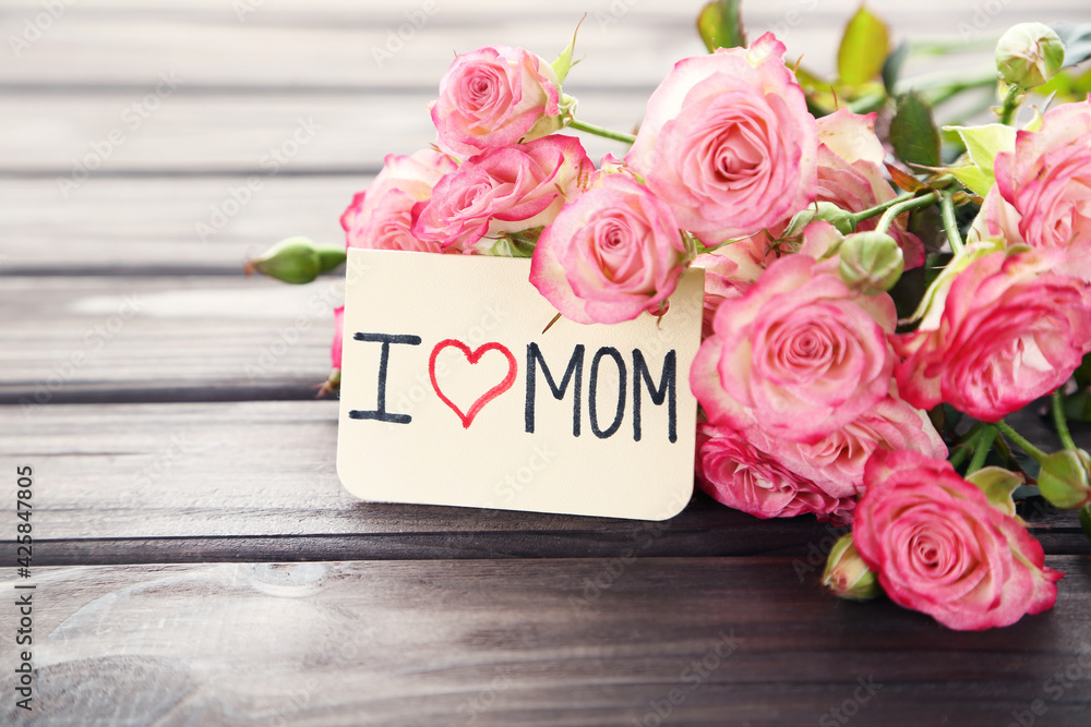 Text I Love MOM with rose flowers on wooden background