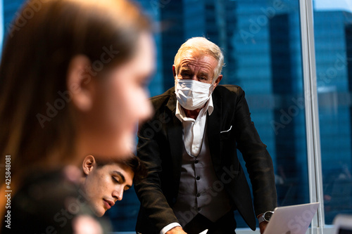 Senior boss in protective mask discussing and brainstorming with employee in meeting room. business people working overtime during Coronavirus