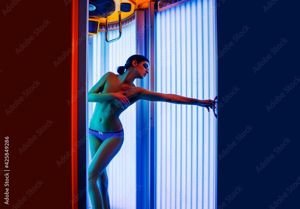 © Volodymyr - Young sexy woman with tan naked healthy body standing in solarium spa salon. Attractive young girl preparing for tanning in solarium.